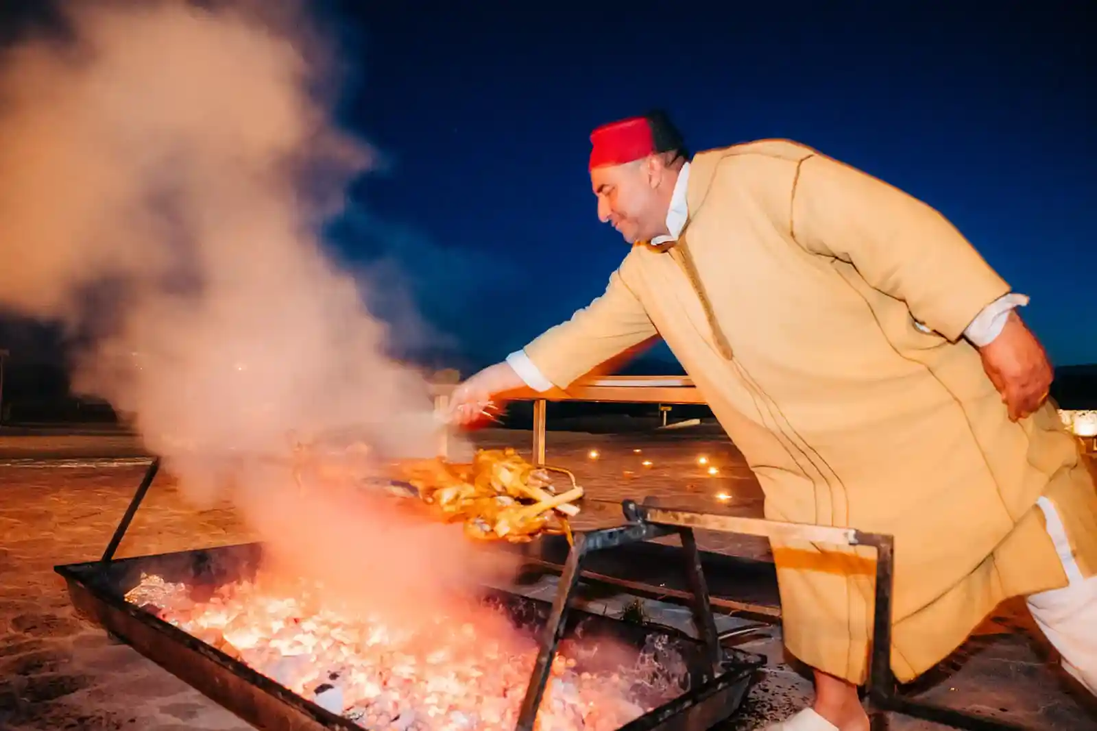 Traditional Moroccan Mechoui Preparation Traditional Moroccan chef preparing Mechoui over coals at night.