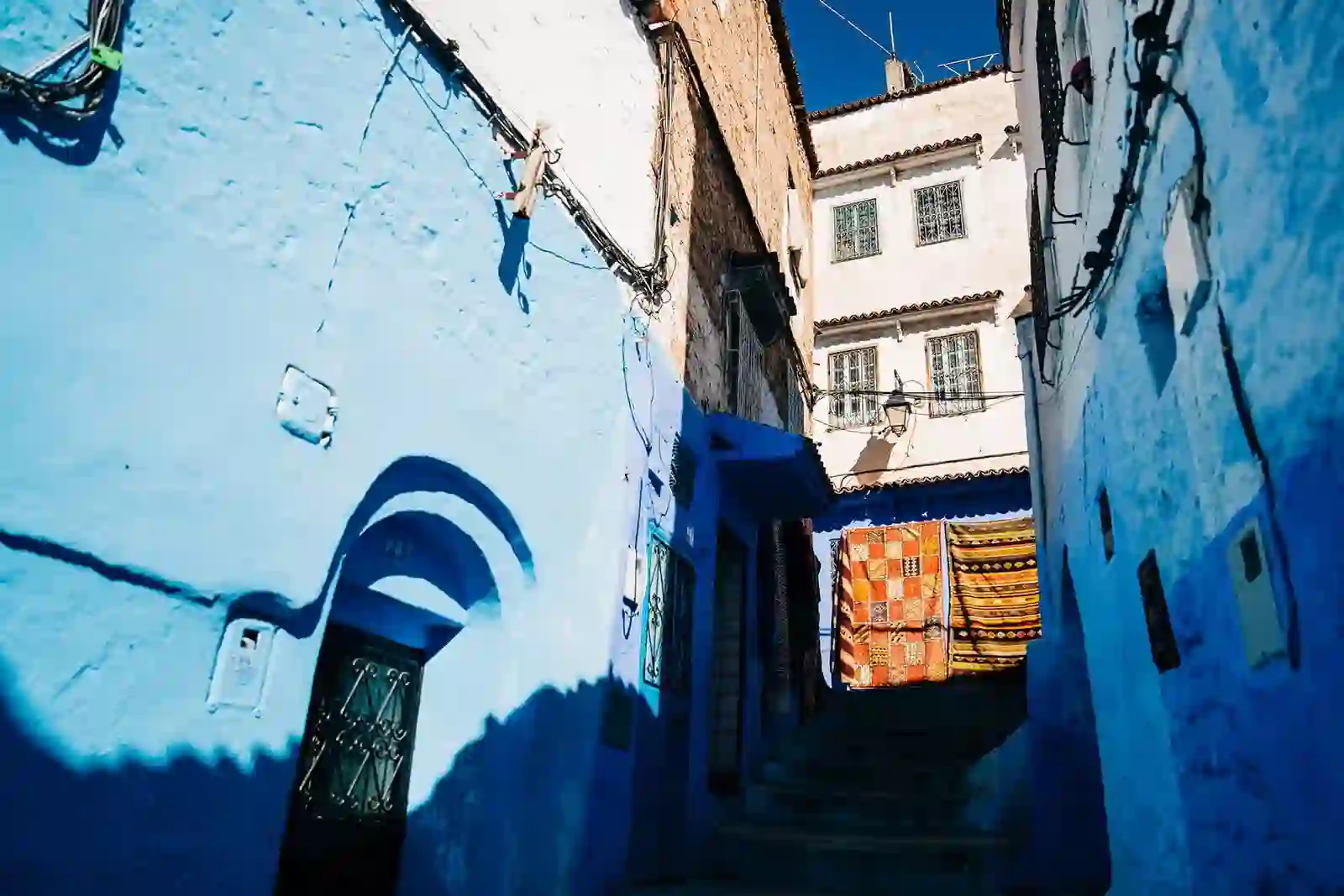 Narrow blue-painted alley in Chefchaouen with a colorful rug hanging in the background.